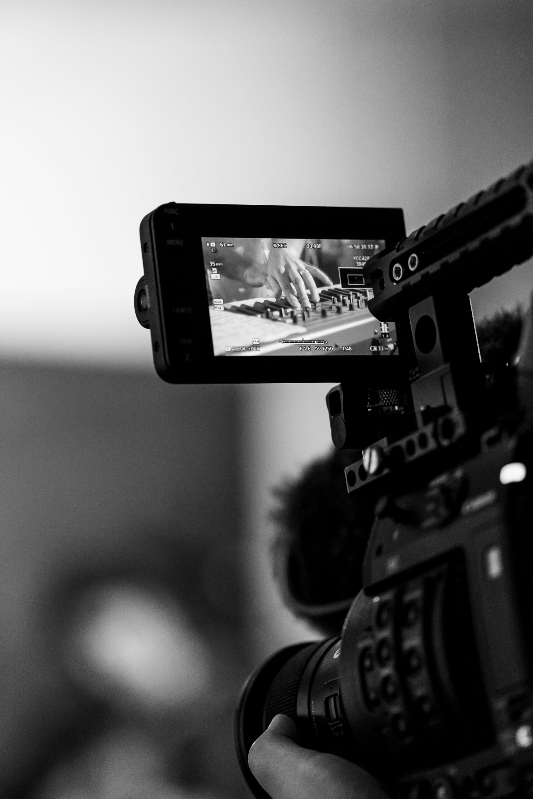 Cinema camera monitor framing a close-up of hands at an audio mixing console